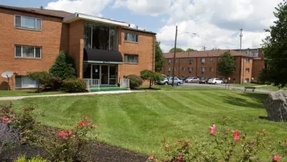 An exterior view of a brick apartment complex with well-maintained green lawns and colorful flowerbeds.