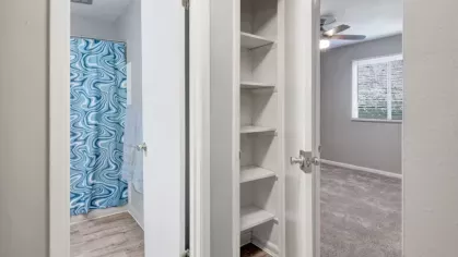 A hallway view showing a bathroom with a blue swirl-patterned shower curtain and an adjacent linen closet with shelves.