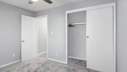 A carpeted bedroom with a white closet door and a ceiling fan, adjacent to a hallway.