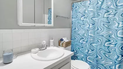 A compact bathroom with a white sink, mirror, and a blue-patterned shower curtain, featuring a tiled countertop.