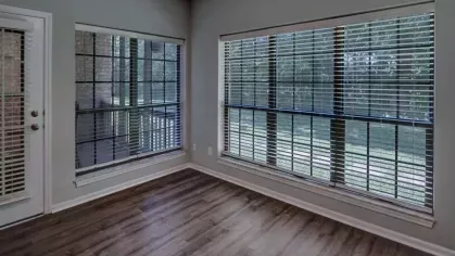 Bright sunroom with large windows featuring white blinds and beautiful views of greenery.