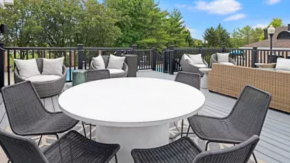 Outdoor seating area with a modern white table, black chairs, and comfortable lounge furniture surrounded by greenery.