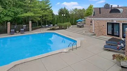 Sparkling swimming pool at Parkhill Luxury Apartments, surrounded by lounge chairs, umbrellas, and brick buildings in the background.
