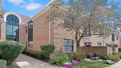 Beautifully landscaped exterior of Parkhill Luxury Apartments with brick buildings, a variety of colorful flowers, and a tree-lined walkway.
