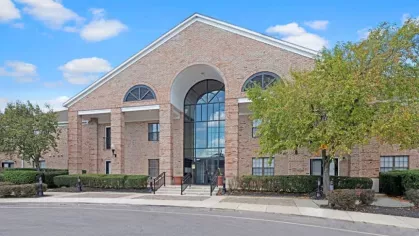 Front exterior of Parkhill Luxury Apartments showcasing a brick facade, arched entryways, and lush landscaping under a clear blue sky.