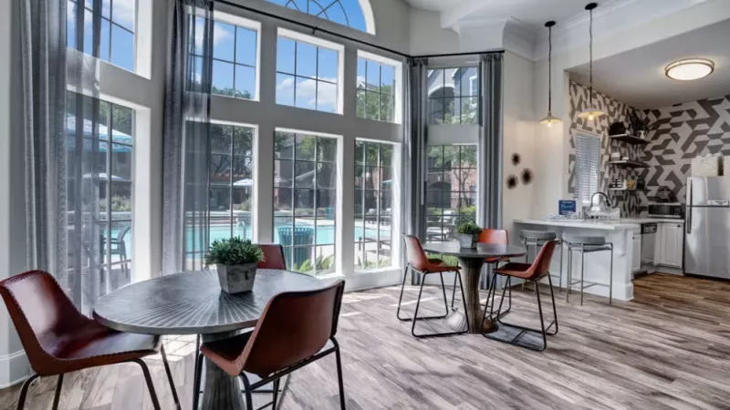 Sunlit dining area with large windows and a view of the pool, featuring a modern kitchen with geometric wallpaper.