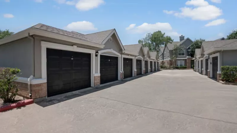 Row of private garages with black doors and a paved driveway in a residential complex.