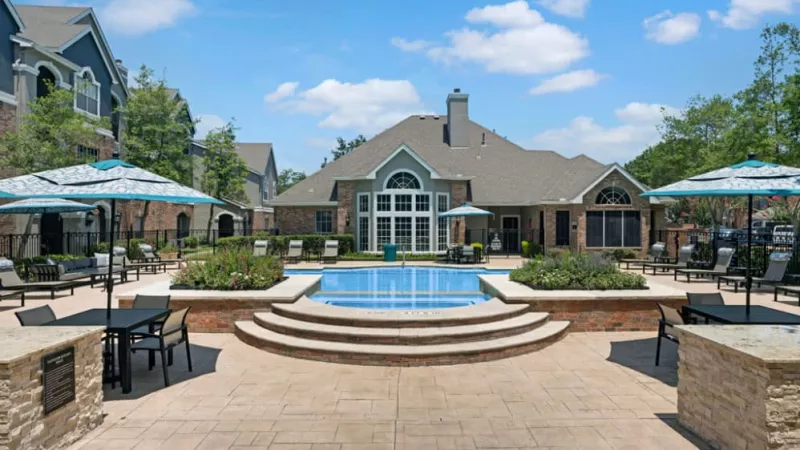 Resort-style pool with surrounding lounge chairs, umbrellas, and a beautifully landscaped patio.