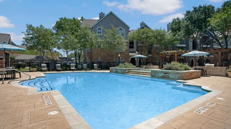Close-up of a sparkling blue pool with a serene courtyard and lush greenery in the background.
