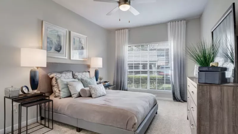 A serene bedroom with soft gray decor, plush bedding, and large windows allowing natural light to flood the room.