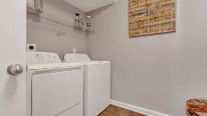 Compact laundry room with a washer and dryer, a wire shelf above, and a framed abstract artwork hanging on the wall.