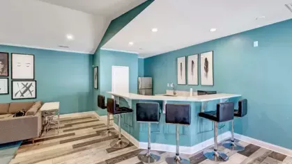 Bar-style seating area in the community clubhouse with a turquoise bar, black stools, and modern framed artwork on the walls.