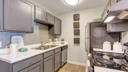 Modern kitchen with gray cabinetry, stainless steel appliances, white countertops, and a tile backsplash in a Residences at West Mint apartment.