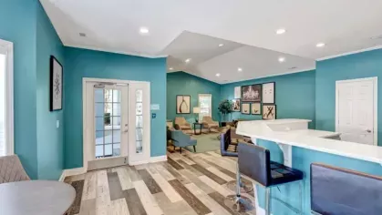 Clubhouse interior with a bar counter, high-top seating, a turquoise wall, and decorative flooring in a wood pattern.