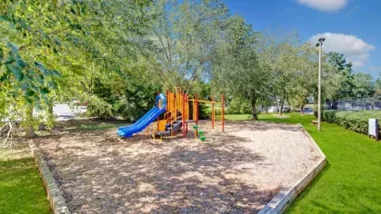 A colorful playground with a slide and climbing structure offers a fun space for children under the shade of trees.