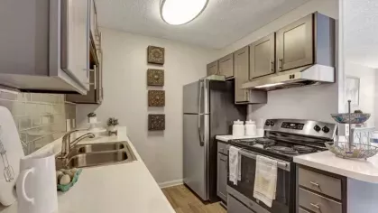 Another angle of the same modern kitchen featuring gray cabinets, a stainless steel refrigerator, stove, and hood. White countertops and light gray backsplash provide a sleek look.