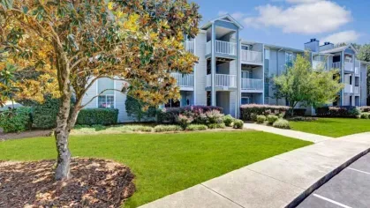 Beautifully maintained apartment buildings with private balconies overlook lush green landscaping and mature trees.