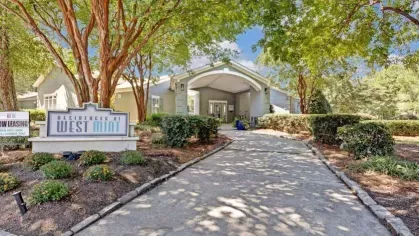 The welcoming entrance to Residences at West Mint, framed by lush landscaping and vibrant greenery.