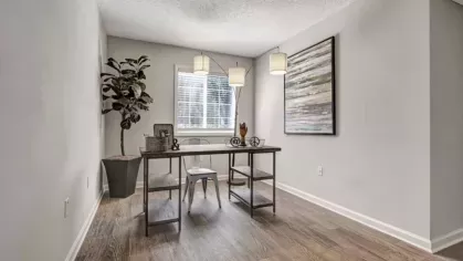 A well-lit home office space with a modern desk, a large potted plant, pendant lighting, and an abstract painting on the wall.