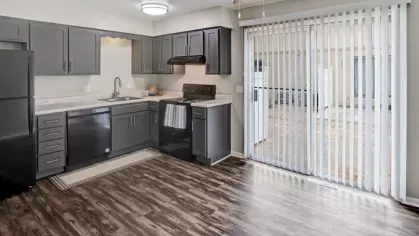 A modern kitchen with sliding glass doors leading to an outdoor area, featuring dark gray cabinets and black appliances.