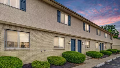 Image of the Apartment Building at Sunset: A row of two-story beige brick apartments with navy doors, illuminated against a vibrant sunset sky.