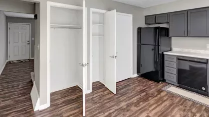 A kitchen with open closet doors showing storage space, featuring dark gray cabinets and black appliances.