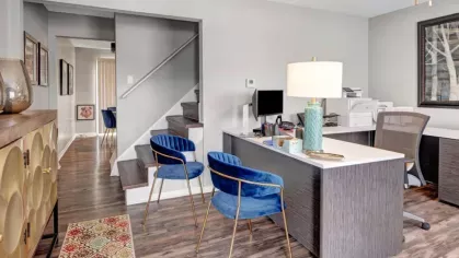 A workspace setup with a modern desk, blue chairs, and stairs leading to the second floor, located in a stylish apartment.