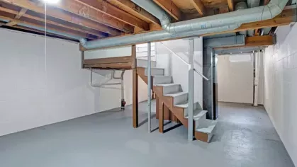 A spacious basement with concrete floors, exposed wooden beams, and a staircase leading to the main level.