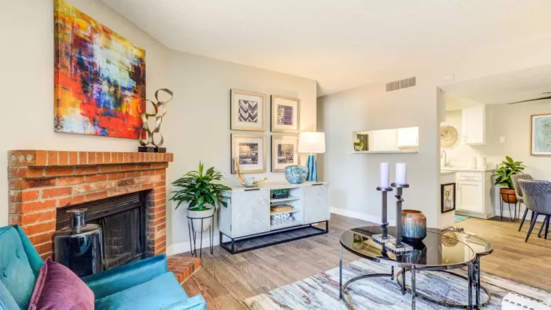 A cozy living room with a vibrant painting, a brick fireplace, and stylish furniture in a neutral-toned setting.