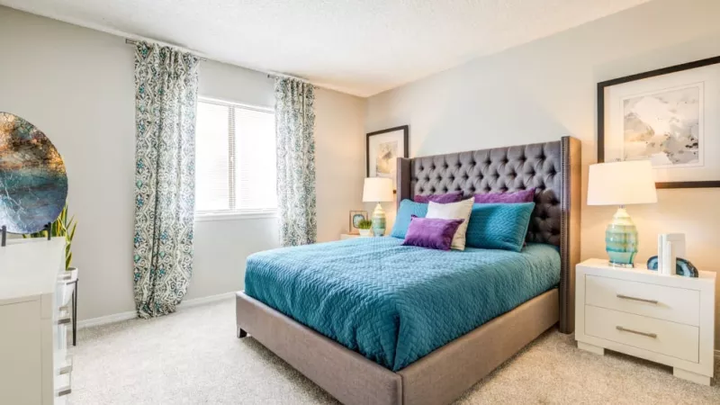 A spacious bedroom with a tufted bed frame, colorful pillows, and decorative curtains enhancing natural light.