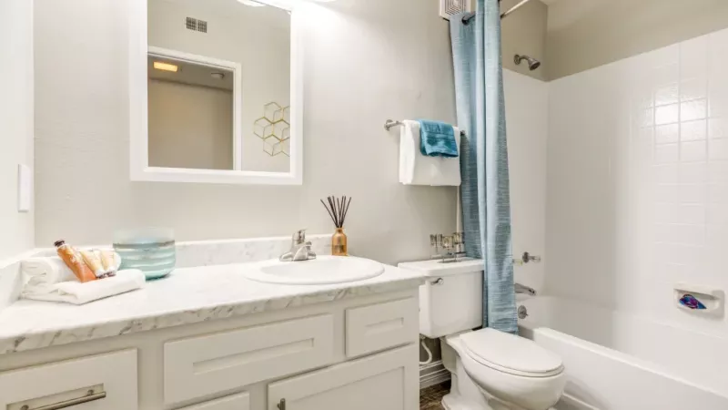 A bathroom with a white vanity, marble countertop, and a shower with blue accents.