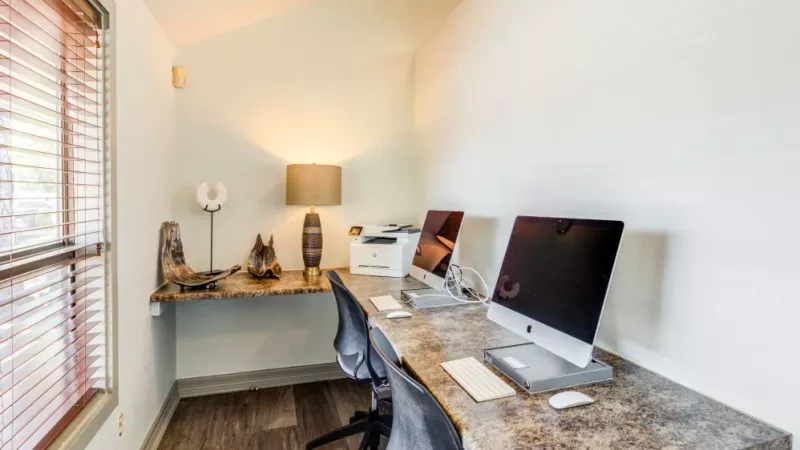 A business center with sleek iMac computers, a printer, and contemporary decor in a well-lit space.