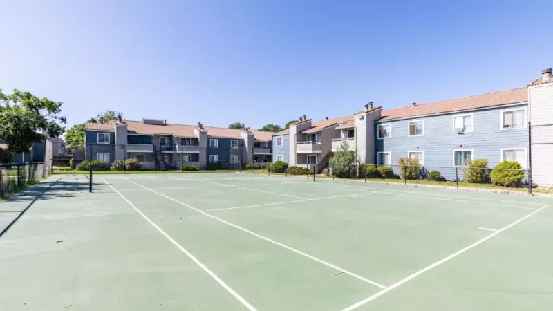 A large outdoor tennis court with apartment buildings in the background.