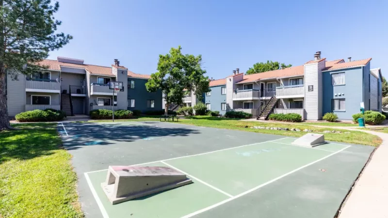 A basketball court surrounded by apartment buildings and green trees.