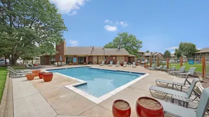 A well-maintained pool area with red ceramic planters and ample seating under a bright blue sky.