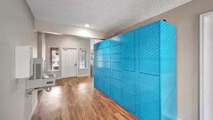 A secure package locker system in a hallway with wooden floors and a bright windowed entrance.