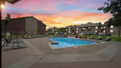 A serene pool area during sunset, surrounded by lounge chairs and residential buildings.
