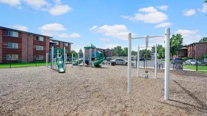 A playground with green slides and swings surrounded by apartment buildings under a sunny sky.