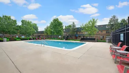 A clean and fenced-in swimming pool area with red lounge chairs and lush landscaping.