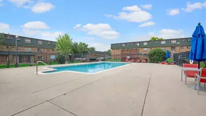 Another angle of the community pool area showcasing blue umbrellas, poolside seating, and nearby apartment buildings.