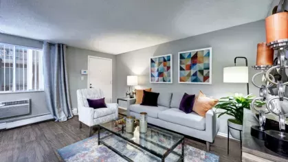 A living and dining area with contemporary furniture, a glass dining table, and a large decorative mirror on a neutral-colored wall.