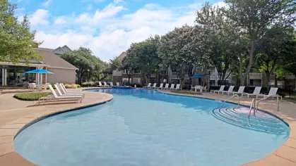 A large outdoor swimming pool surrounded by lounge chairs, umbrellas, and blooming trees for a relaxing atmosphere.