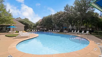 Another view of the pool area, showing curved steps leading into the water, lounge seating, and shaded patio areas.
