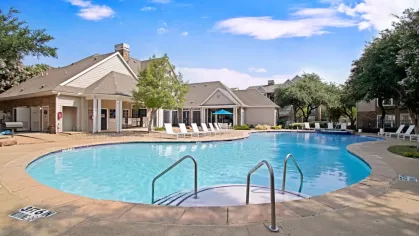 A luxurious swimming pool surrounded by lounge chairs, located in front of a clubhouse on a bright, sunny day.