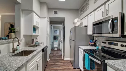 A contemporary kitchen with stainless steel appliances, granite countertops, and white cabinets leading to a bathroom.
