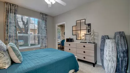 A different angle of the same bedroom, featuring a dresser, decorative vases, and a large window with patterned curtains.