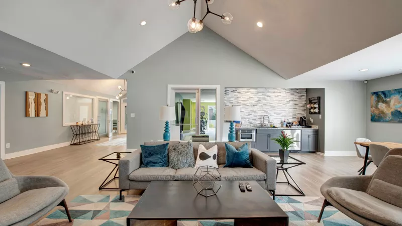 A stylish clubhouse lounge with contemporary furniture, vibrant decor, and a kitchenette in the background.