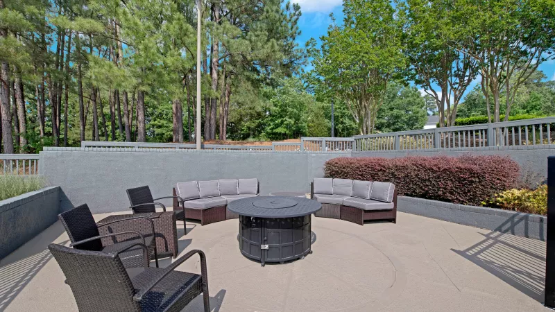 A cozy outdoor seating area with a firepit, surrounded by trees and manicured shrubs.