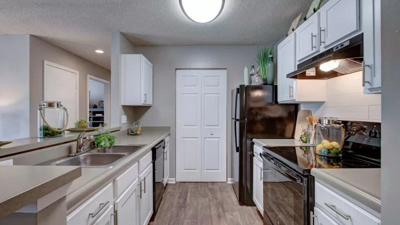 A modern kitchen with white cabinets, black appliances, and a sleek countertop featuring decorative accents.