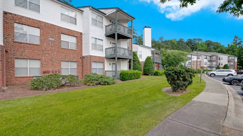 A side view of apartments with balconies and a neatly landscaped lawn.